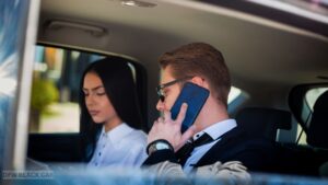 Business professionals working and reviewing documents in the backseat of a chauffeur-driven luxury car, focused on a client presentation while traveling through the city.